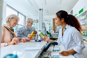 Obraz premium Happy senior couple buying vitamins with help of female pharmacist in drugstore.