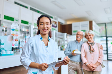 Happy Chinese pharmacist at work with her customers in background.
