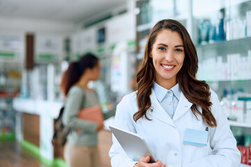 Happy female pharmacist working in pharmacy and looking at camera. - obrazy, fototapety, plakaty