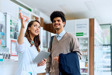 Happy pharmacists assists her male customer in pharmacy.