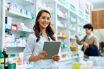Happy female pharmacist with touchpad working in pharmacy and looking at camera.