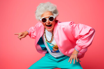 Portrait of a funny grandmother in 80s dance attire with sunglasses on a pink background.