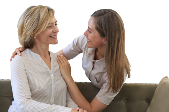 Beautiful middle aged mom and her adult daughter are hugging and smiling while sitting on couch on a transparent background