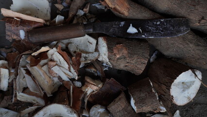 a large knife with a wooden handle, placed on a pile of cassava, peeled skin, the pile of cassava with skin that has been peeled