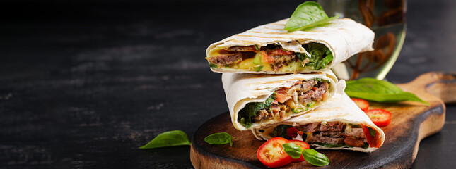 Grilled tortilla wraps with beef and fresh vegetables on wooden board. Beef burrito. Mexican food. Healthy food concept. Banner - obrazy, fototapety, plakaty