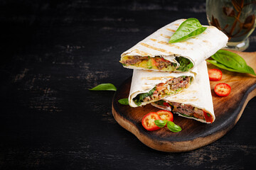 Grilled tortilla wraps with beef and fresh vegetables on wooden board. Beef burrito. Mexican food. Healthy food concept.