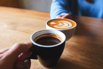 Closeup image of a couple people clinking coffee cups together in cafe
