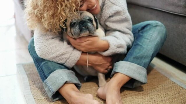 One female owner bonding her old pug dog at home sitting on the floor. Concept of love and affection for animals. Domestic lifestyle with puppy. Together best friend aged pet. One woman and dog