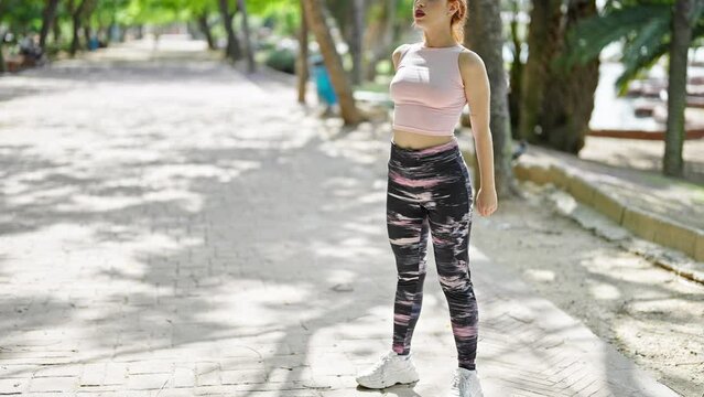 Young redhead woman wearing sportswear training legs exercise at park