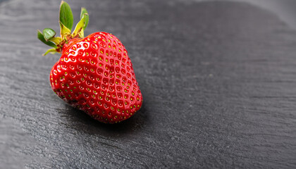 A close up macro photograph of a whole fresh ripe organic strawberry on a dark black slate stone background with copy space.