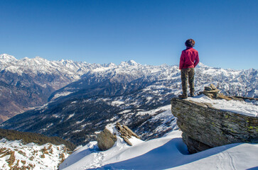 Fototapeta premium man standing on the top of a mountain looking towards the snow covered mountain ranges in the himalayas