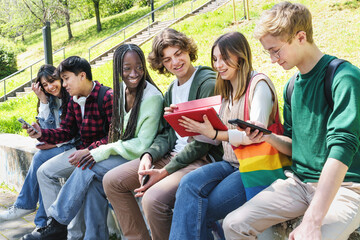 Multicultural Teenagers Interacting at School Park - Diverse teens sit on a wall, conversing and using mobile devices.