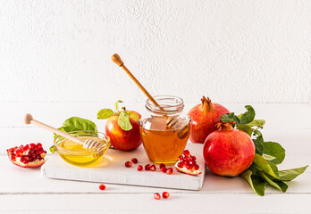 A composition of a jar and a bowl of different honey on a wooden board with ripe pomegranates and apples. wooden table. Roshhashan holiday.