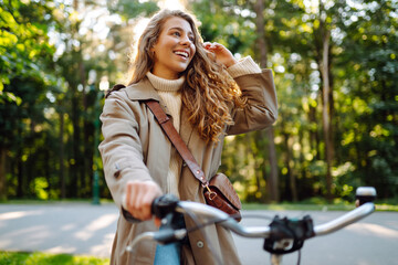 Fototapeta na wymiar Happy pensive young woman in stylish clothes riding a bike in a sunny park, outdoors, looking away. Active lifestyle. The concept of nature.