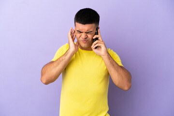 Young handsome man using mobile phone over isolated purple background frustrated and covering ears