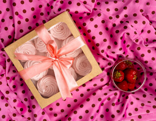 homemade marshmallow zephyr with strawberry taste in box, pink dotted textile, picnic style. woman hand taking one piece. fruits in glass bowl green grass