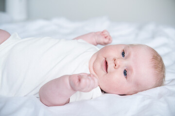 healthy smiling baby lies on his back on bed on white bedding