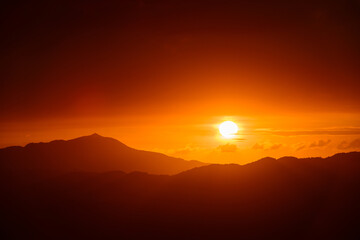The orange-red sunset is covered by clouds as it moves towards the horizon. View of the urban landscape from Dajianshan Mountain, New Taipei City.