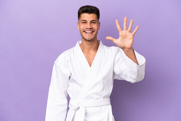 Young caucasian man doing karate isolated on purple background counting five with fingers