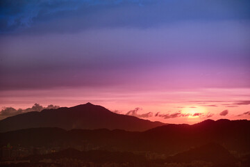 Obraz premium The orange-red sun emerged from the clouds and moved toward the horizon. View of the urban landscape from Dajianshan Mountain, New Taipei City.