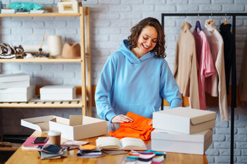 Clothing store: young happy woman, small business owner, seller using tablet checks and packs...