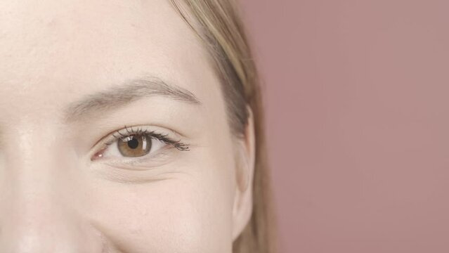 A woman's eye close up. Cropped shot of woman's face in studio on pink background. Good vision and eye care. Contact lenses. Cosmetic line for eye contour care. HDR BT2020 HLG Material.