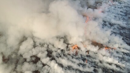 Flying over wildfire and plumes of smoke. Natural disaster due to extreme heat and climate change. Aerial view of big smoke clouds and fire on the field. Grass fire aerial shot. Big smoke clouds and - 628454191