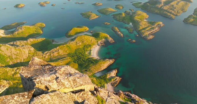 Pointed rocks overhang arctic Rod&oslash;ya beach in midnight sun morning glow; drone