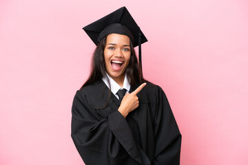 Young university Colombian woman graduate isolated on pink background surprised and pointing side