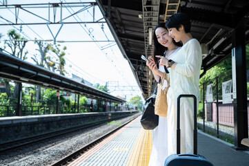 Young Asian women tourists cheerfully waiting for the train at the station. Travelling on public transportation