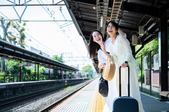 Young Asian women tourists cheerfully waiting for the train at the station. Travelling on public transportation