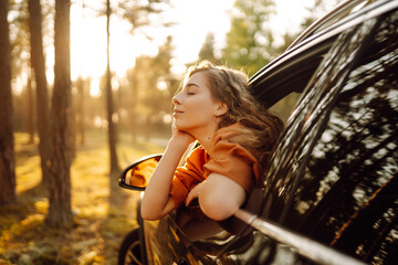 Feeling of freedom on beautiful sunny summer road. Shot of an attractive woman leaning out of car...