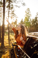Fototapeta na wymiar Feeling of freedom on beautiful sunny summer road. Shot of an attractive woman leaning out of car window while driving. Active lifestyle, travel.