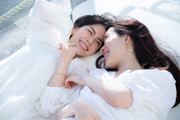 Young Asian females having fun at a seaside restaurant terrace, smiling joyfully	
Friendship and vacation lifestyle.