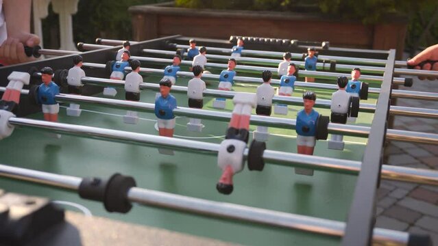 Outdoor kicker board game match with football player figurines control, static shot. Teenagers vigorously spin axes with players and hit ball, passing and kicking the goal in game of table soccer.