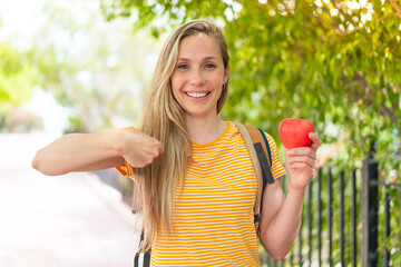Young blonde woman with an apple at outdoors with surprise facial expression