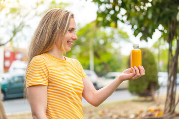 Young blonde woman holding an orange juice at outdoors with happy expression
