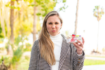 Young blonde woman holding a three dimensional puzzle cube at outdoors with sad expression