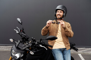 Stylish smiling confident man, biker wearing helmet standing near sport motorcycle. Handsome...