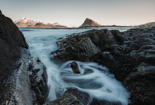 Rocky coast with waterfall against snowy mountain and sky
