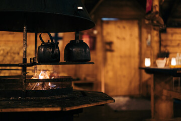 Metal kettles on hot plate with fire in kitchen with blurred interior