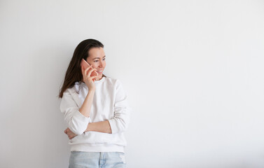 Young woman talking on mobile phone, smiling, using social media. Millennial person in white sweatshirt on white background. People using technology. Work call.