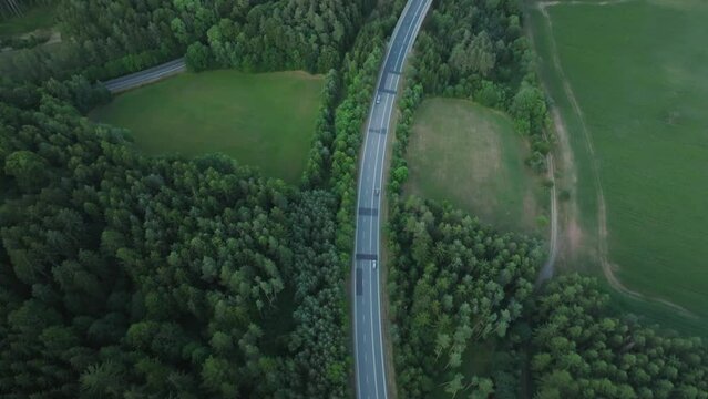 Cars passing on a road surrounded by green forests in summer. A drone view of traveling in the Czech Republic