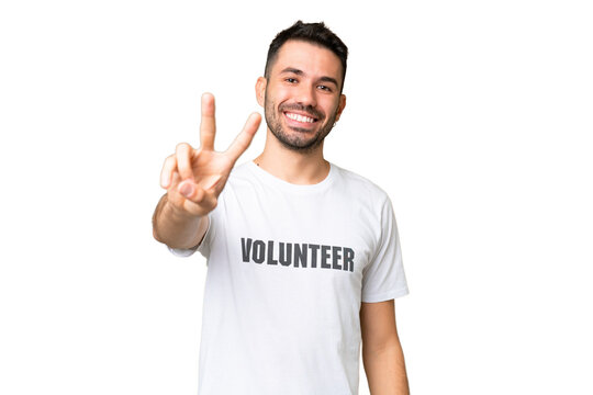 Young volunteer caucasian man over isolated chroma key background smiling and showing victory sign