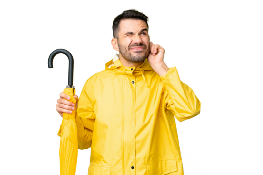 Young caucasian man with rainproof coat and umbrella over isolated background frustrated and covering ears