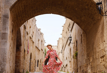 summer trip to Rhodes island, Greece. Young Asian woman in ethnic red dress walks Street of Knights...