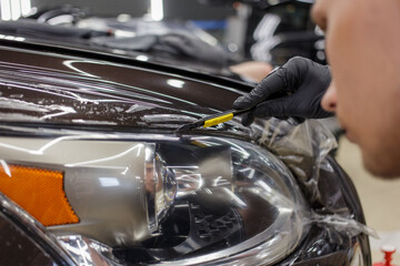 The process of installing a protective polyurethane film for paint on the front headlight of a car.