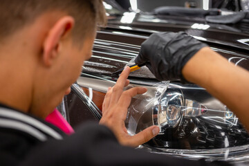 The process of installing a protective polyurethane film for paint on the front headlight of a car.