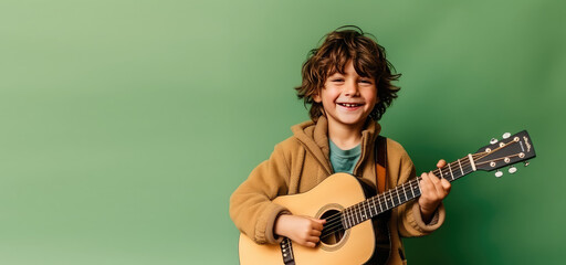 Joyful child playing guitar isolated on flat green background with copy space. Creative banner for...