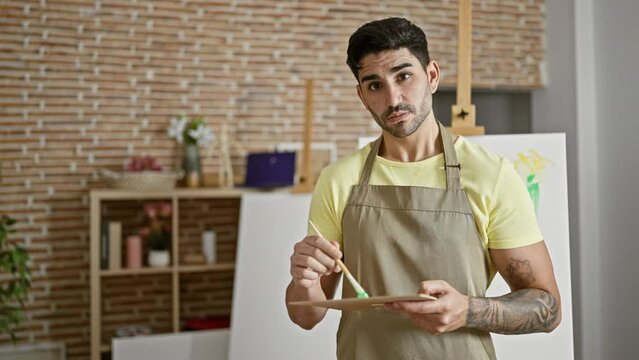 Young hispanic man artist smiling confident mixing color on palette at art studio